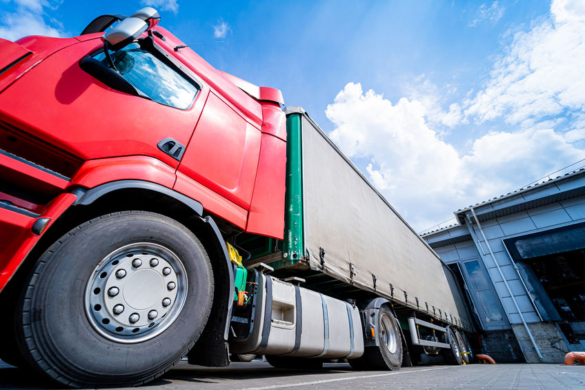 Large trucks near warehouse against blue sky background.